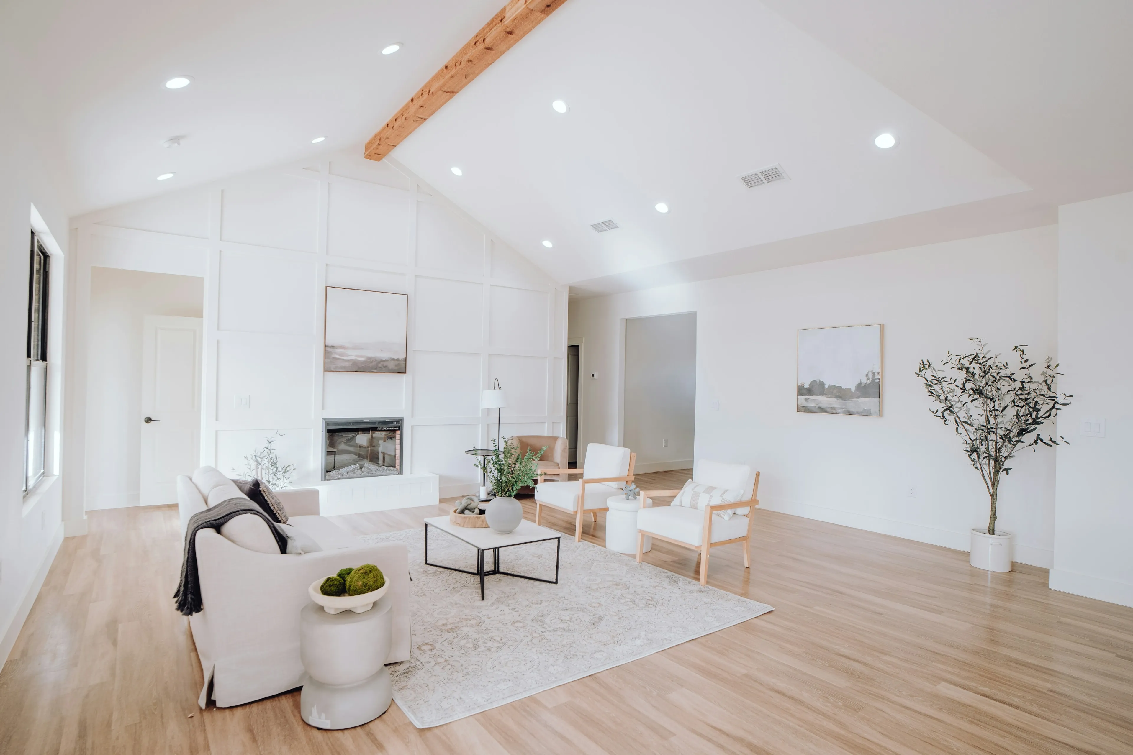Living room under a vaulted ceiling with a timber beam, white armchairs and a fireplace