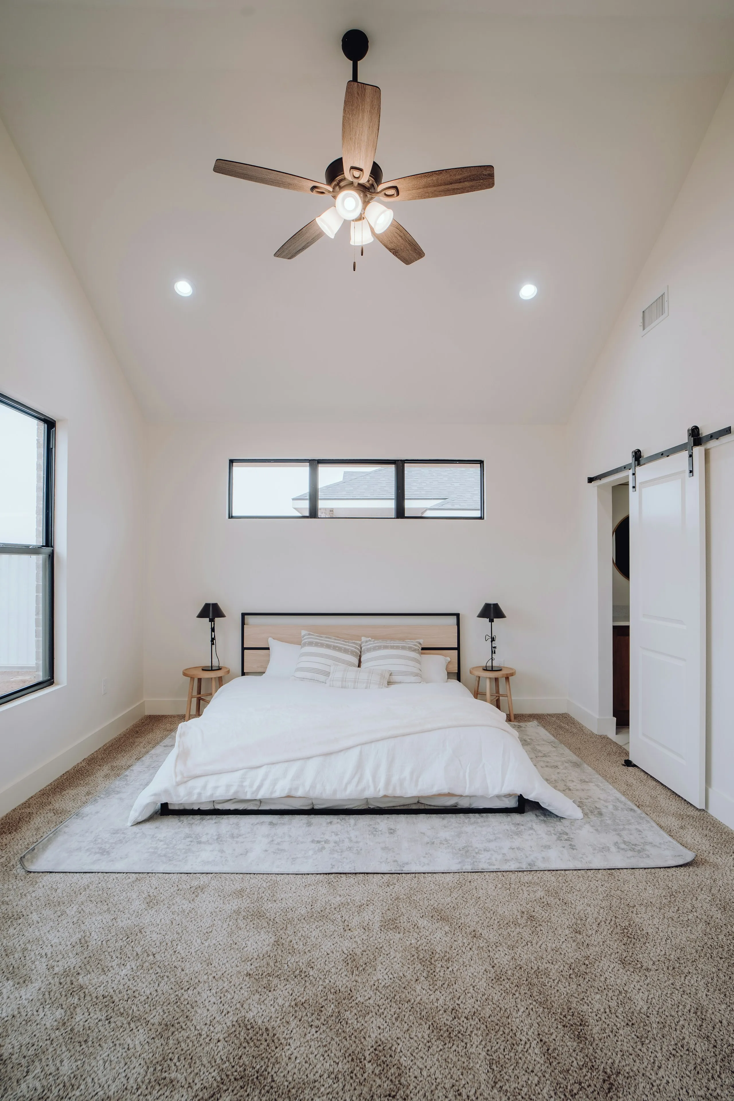 Bedroom under a vaulted ceiling with a ceiling fan and a low white bed