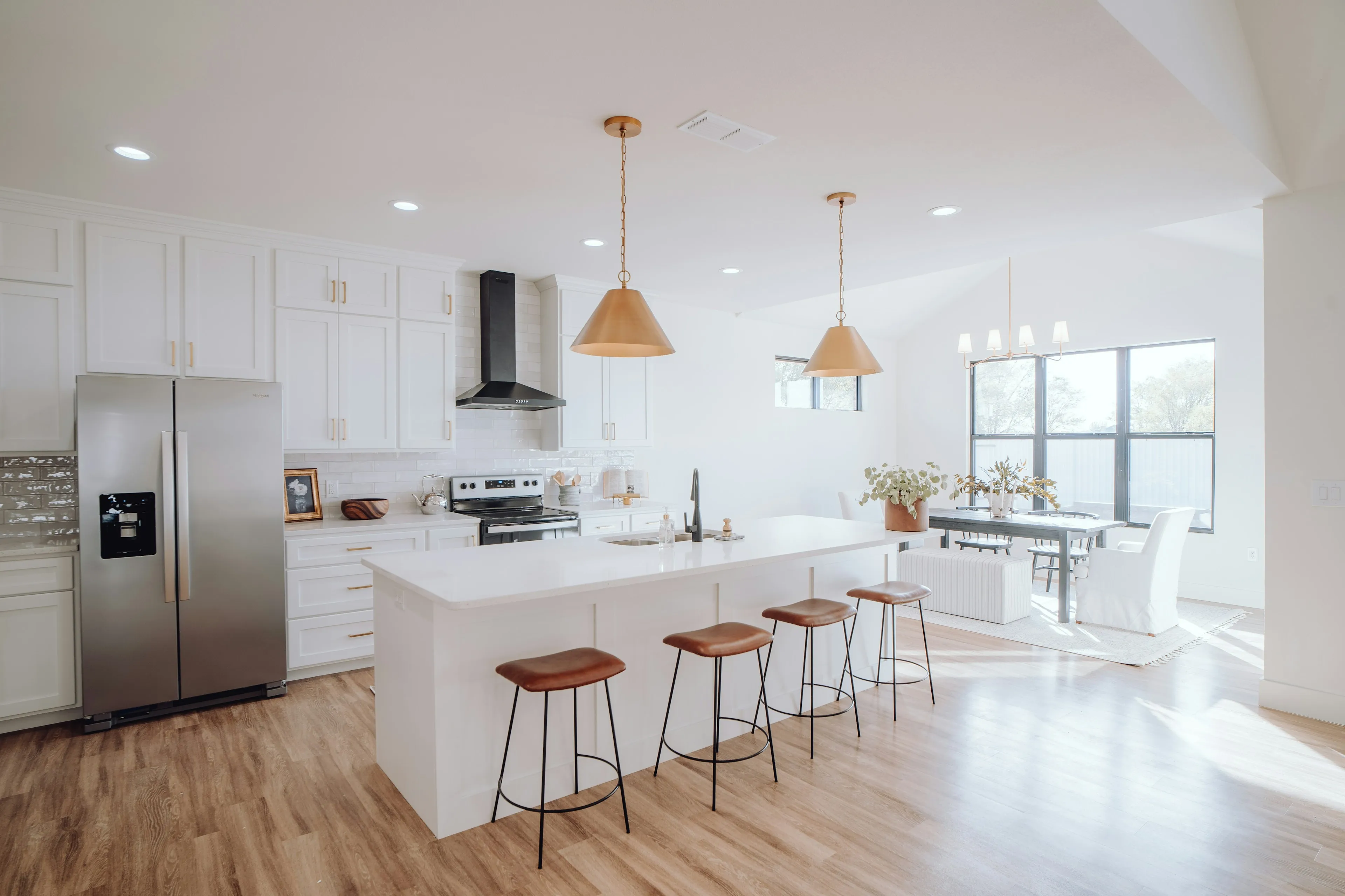 Bright open kitchen with a white island, wooden bar stools and copper pendant lights